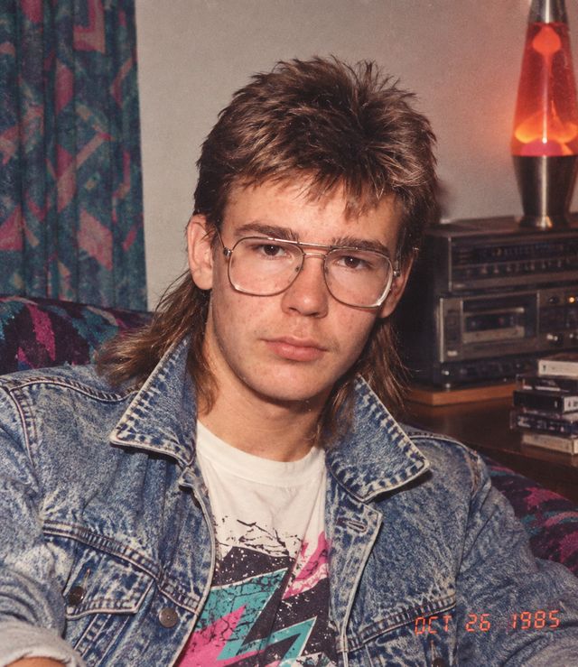 Tommy Cape at home: mullet, gold aviator glasses and an acid-wash denim jacket, a lava lamp and a cassette deck behind him.